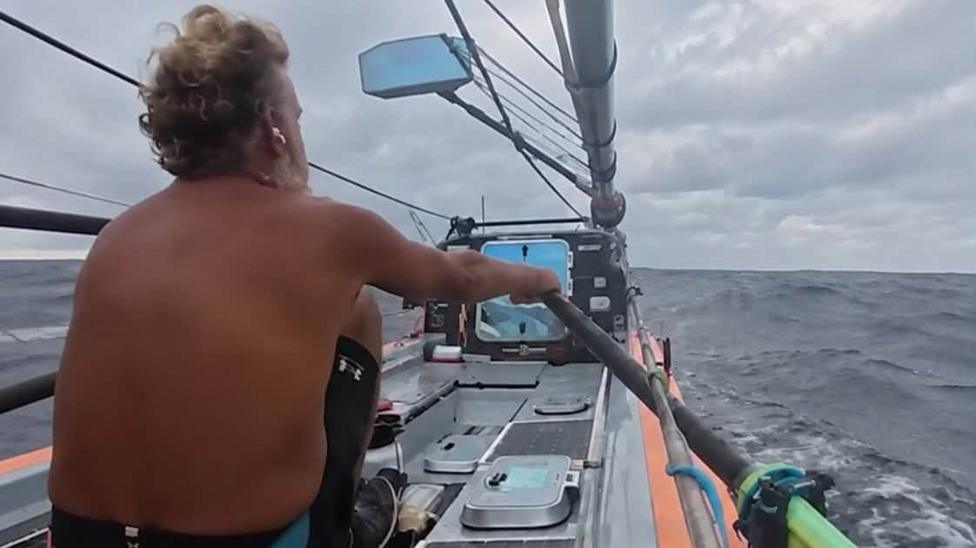 View from behind Dave Bell's sea as he rows in the middle of the ocean. He is wearing no shirt and the sea and sky are grey