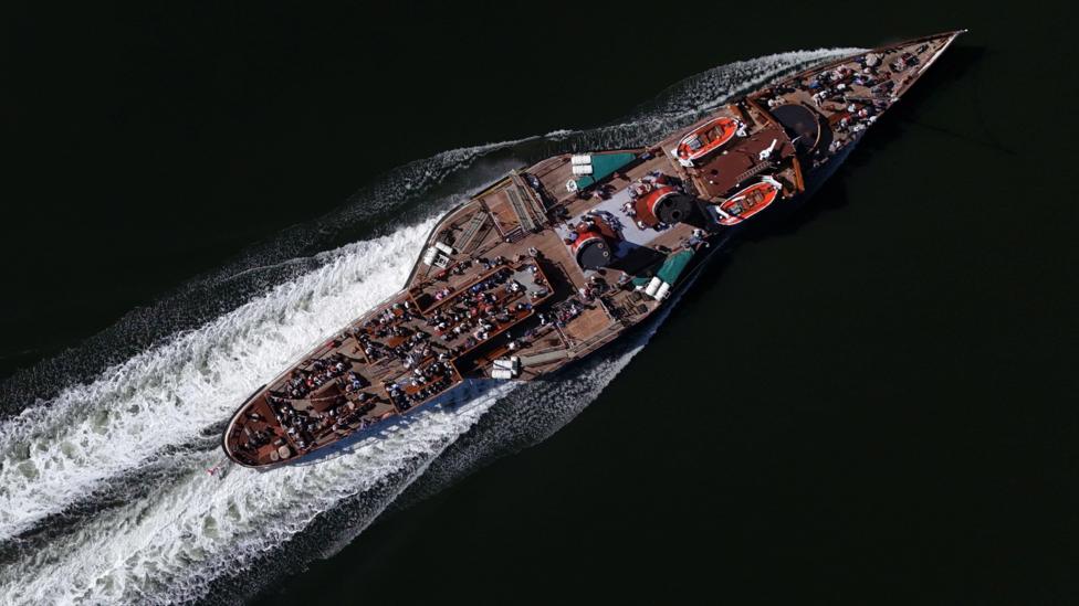 Aerial view of the historic paddle steamer Waverley cruising through dark water, with passengers on deck and a white wake trailing behind the vessel.
