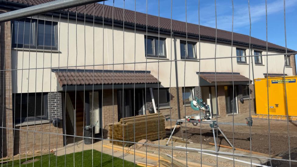 A row of newly built houses behind a fence.