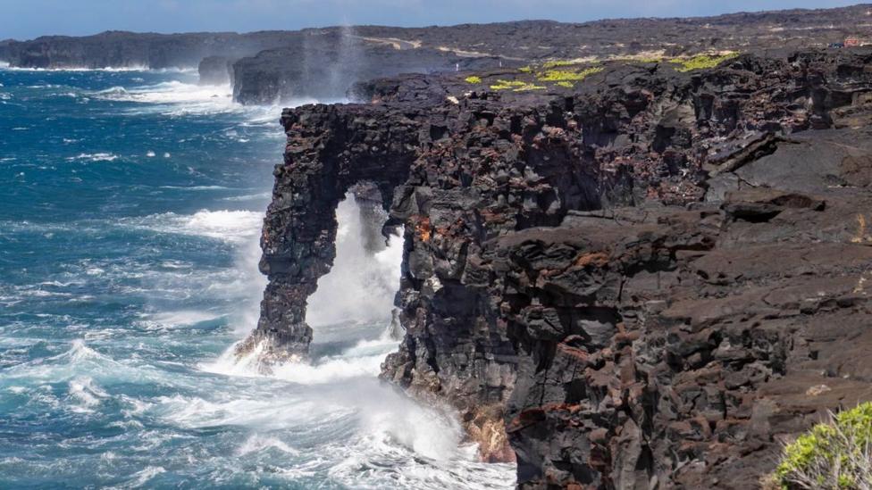 The sea arch still standing, protruding out from a rocky cliffside over the ocean waves