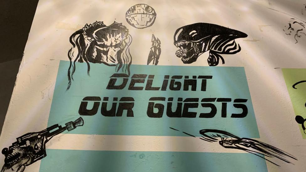 A wall painting saying "delight our guests" with various figures from Star Wars, Star Trek and Alien drawn on the wall
