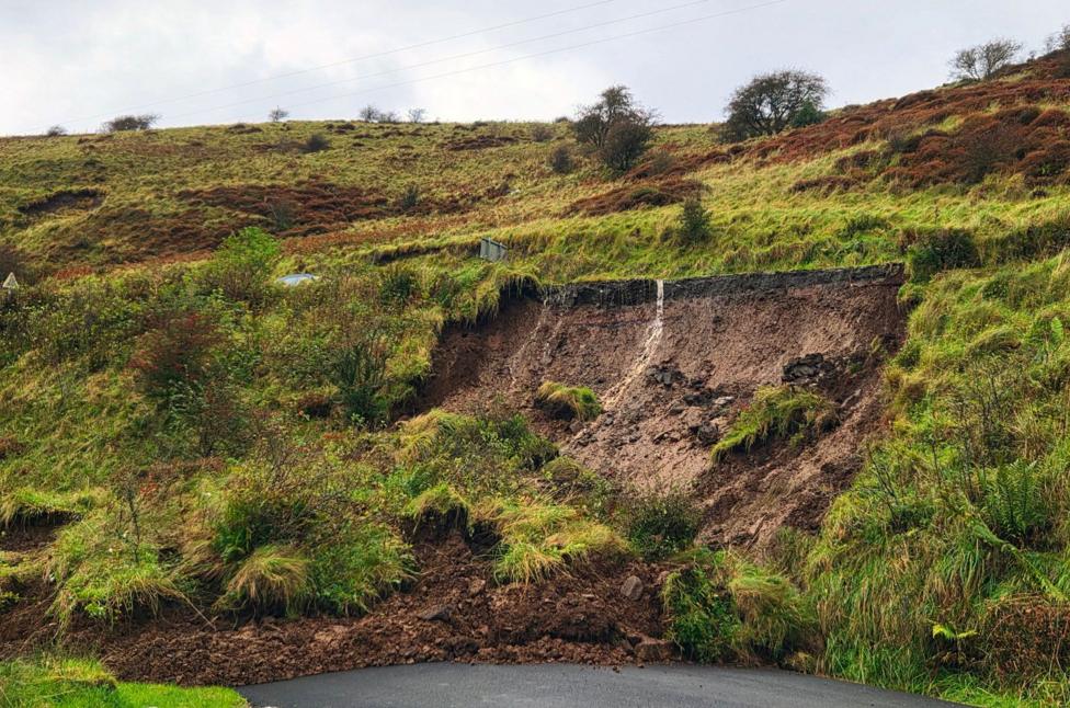 A large amount of soil, grass and rocks blocking a road