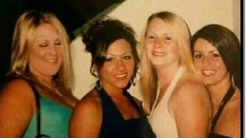 Four women smile at the camera, the photo is low quality and likely taken on an early digital camera. The woman on the left has blonde hair and is wearing a turquoise top, next to her is a woman with brown hair piled up in an up-do and she is wearing a black top. Next to her is a woman with blonde hair and she is wearing a pink top, next to her is a woman with brown hair and she is wearing a black top.