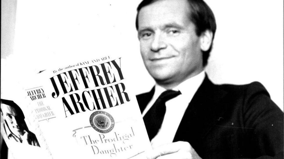 Jeffrey Archer holding up The Prodigal Daughter, one of his books