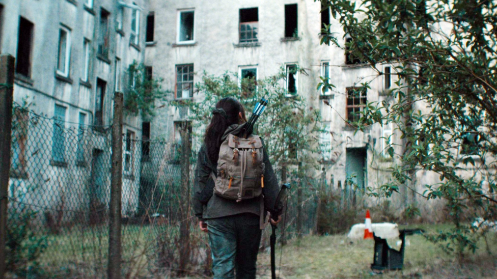 Jade McDonald walks through an abandoned area of Clune Park. She is dwarfed by grey, abandoned tenements.