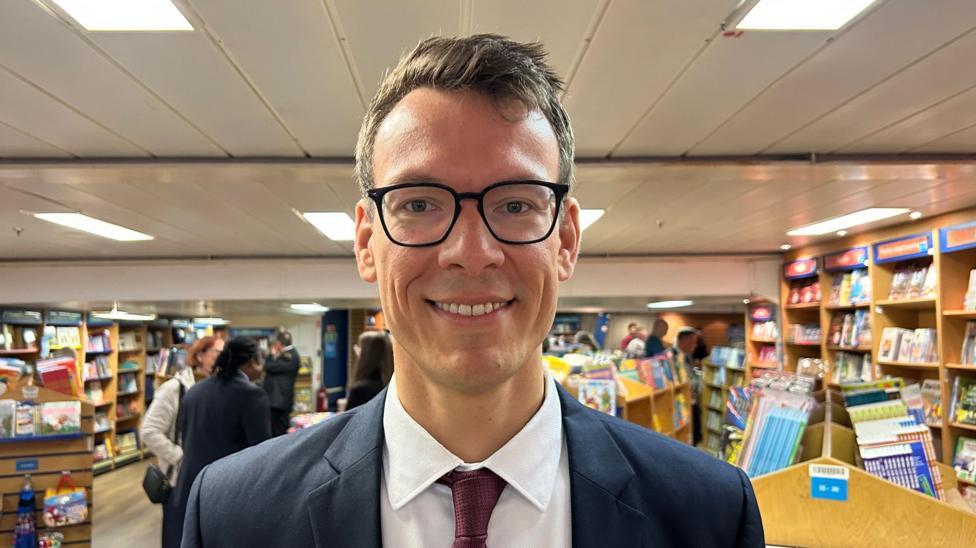A man with brown hair and brown rimmed glasses