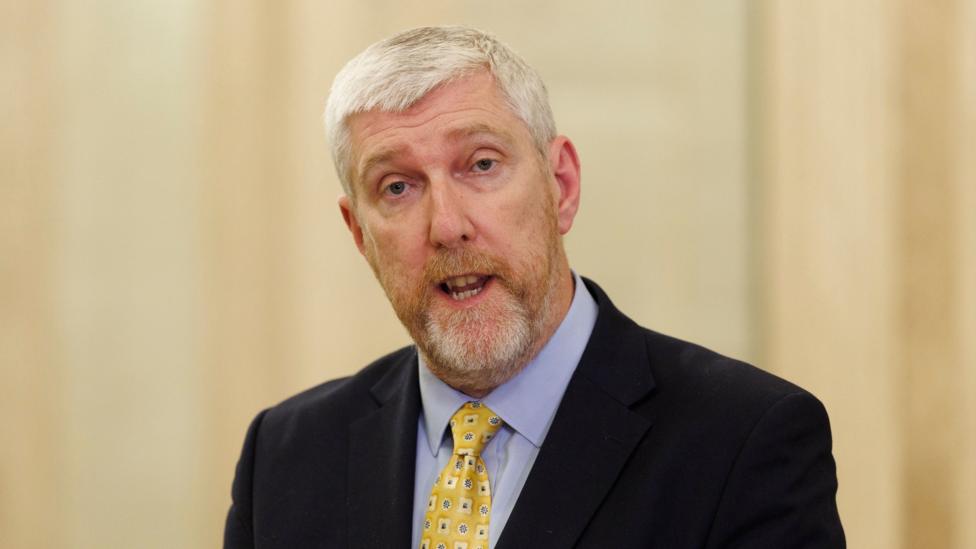 John O'Dowd. He has short white hair and beard, wearing a dark blazer, light blue shirt and yellow tie.
