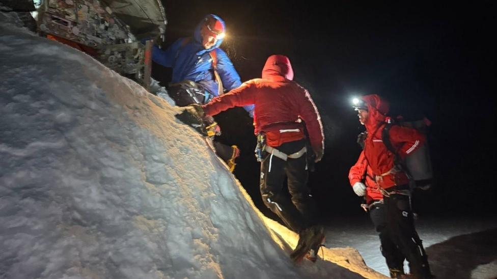 Lochaber MRT volunteers out in a call-out in snow and the dark. The team are wearing brightly coloured outdoor jackets and head torches.
