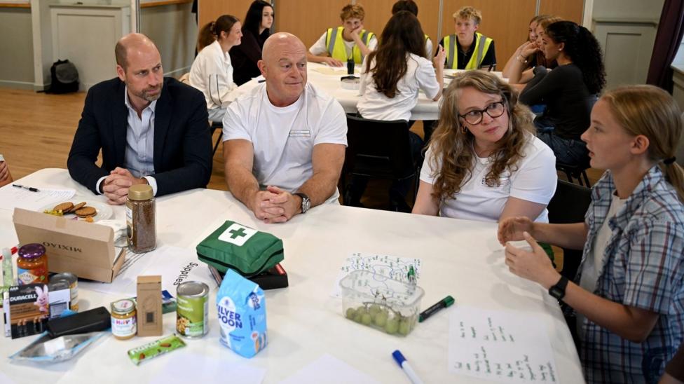 Prince William and Ross Kemp sit at a white table as they talk to two young people
