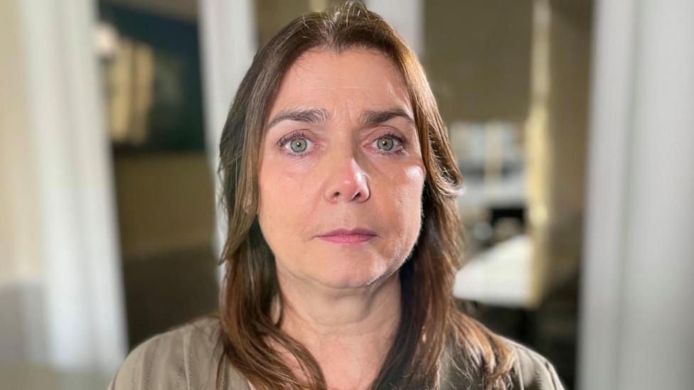 Tracy Brown has long, brown hair and is looking sternly at the camera