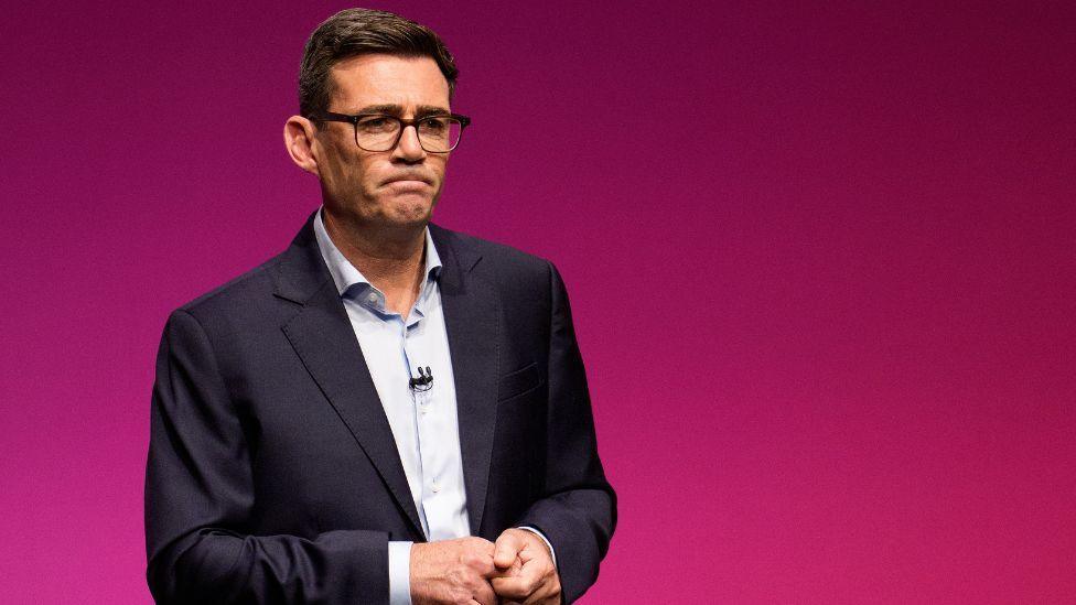 Andy Burnham, who has short dark hair and glasses, wearing a business suit 