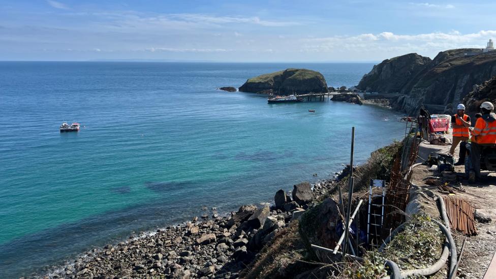 People in hi-vis working on the landslip on the coastline. To the left is the sea.