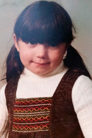 An old portrait picture of Tracy Lewis as a young girl. She has dark hair tied in pigtails and a long fringe, and is wearing a white top and a brown dress.