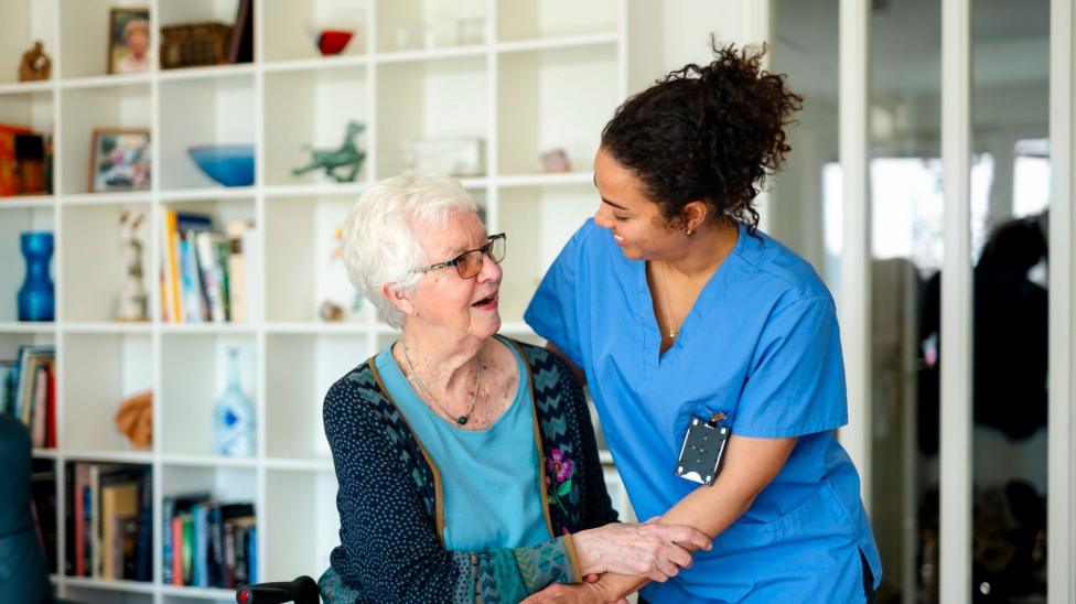 Elderly woman sitting on rollator while spending leisure time with female caregiver at home