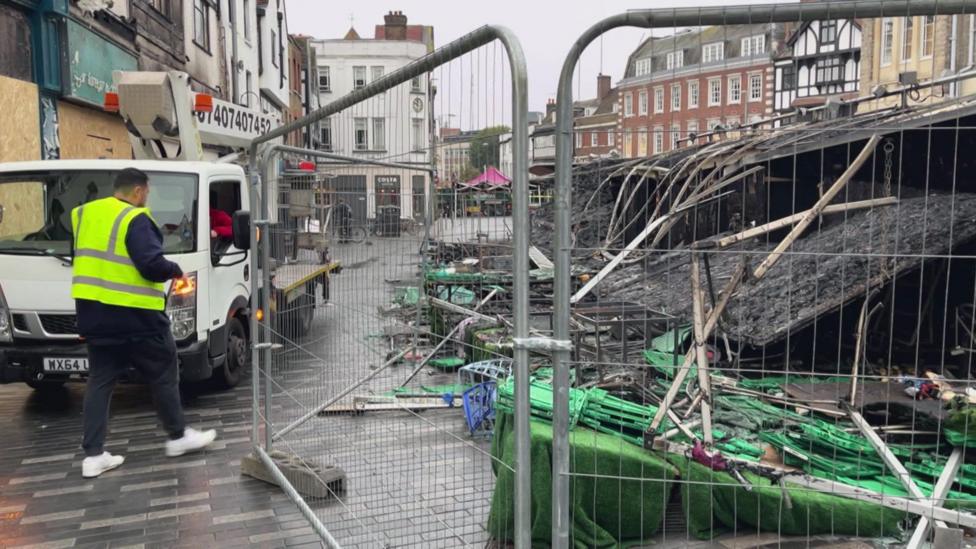 Man opens temporary metal gate near burnt down market stalls