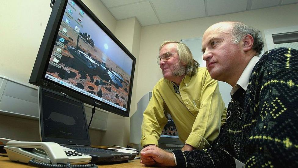 Pillinger is with another scientist looking at a computer screen with Beagle 2 display as a desktop background