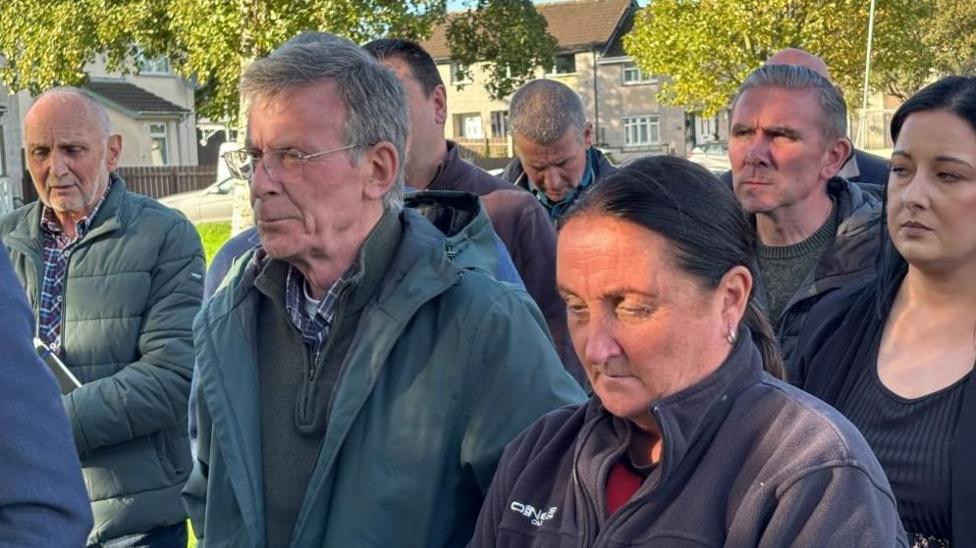 A group of people standing adjacent to the camera - Breandán Mac Cionnaith and Linda O'Neill are in the foreground. He's wearing a green coat and she's wearing a black fleece.