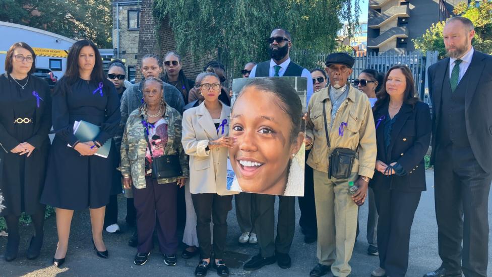 A group of people wearing purple ribbons hold a large image of Mia.