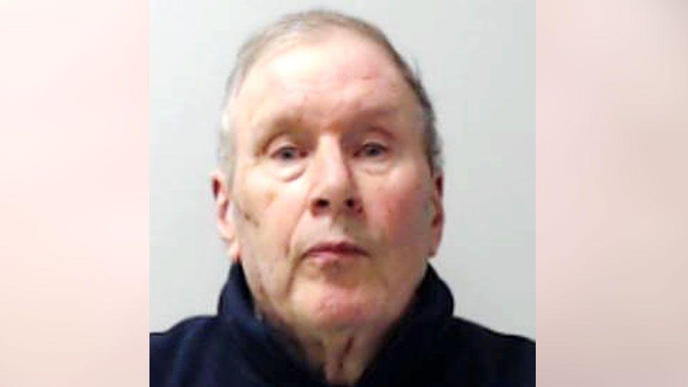 A police mugshot of Christopher Harrisson. He is an older man with thinning grey hair. He is wearing a blue fleece-like top as he stares into the camera.
