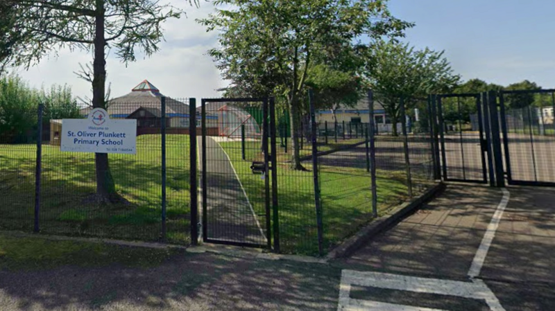 An exterior shot of St Oliver Plunkett Primary School, in Strathfoyle, County Londonderry. The school is white and blue and has a large pyramid-shaped window on its roof.