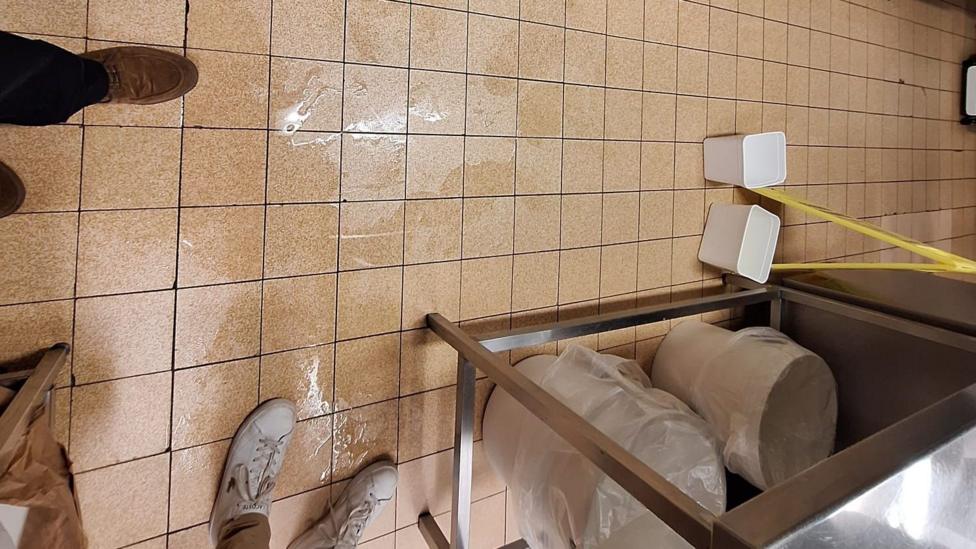 A number of people stand round a wet floor and a number of buckets are visible beside them