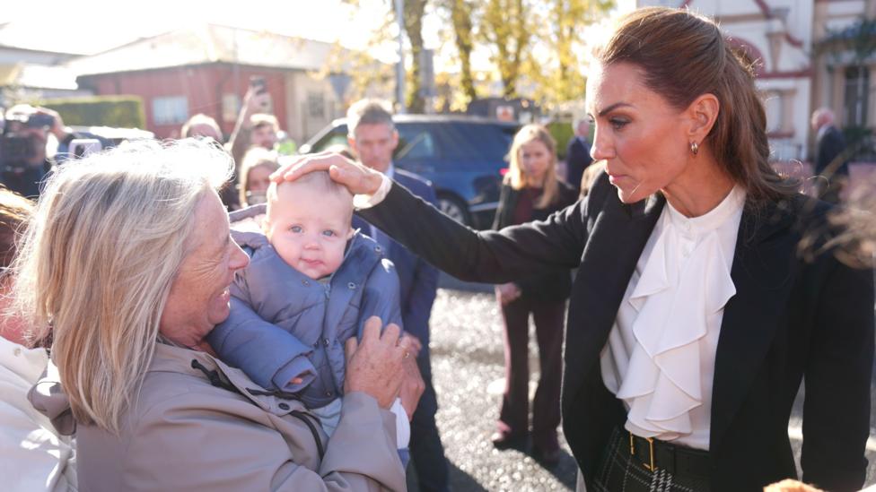 A woman with dark hair pats a baby on the head