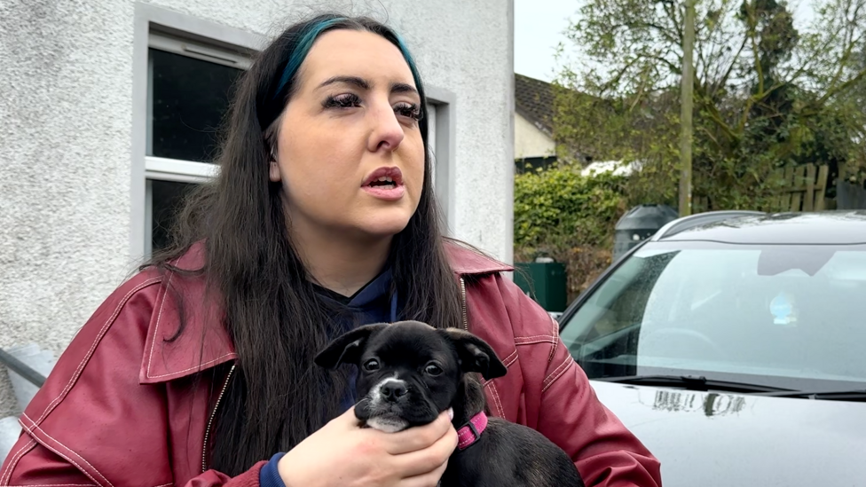Kerry Louise holds a black squashed-faced dog. She has a red leather jacket on.