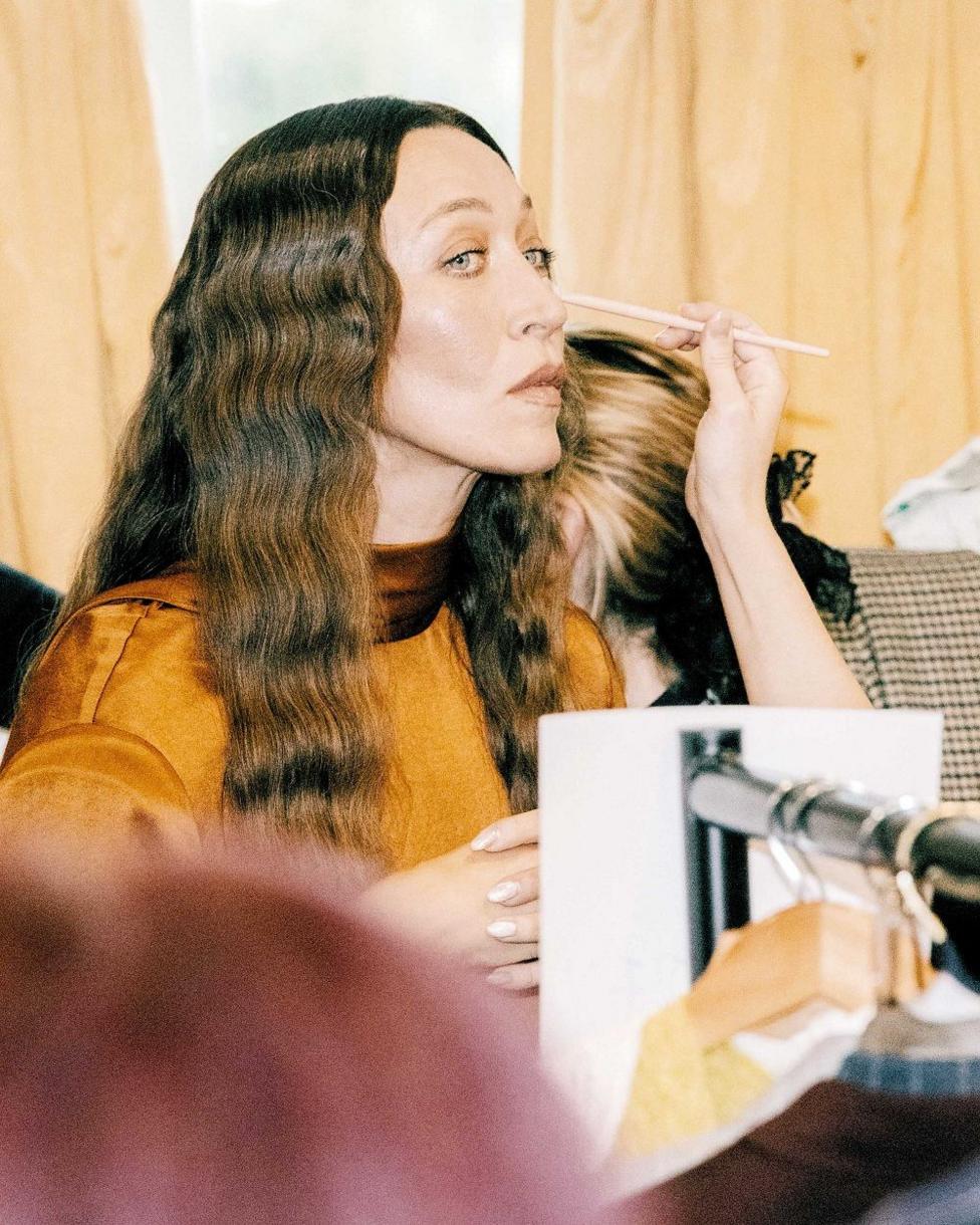 A close shot of a woman in an orange top, having her makeup applied