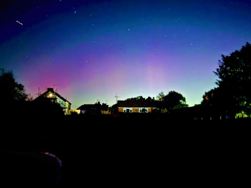 An image of the sky in Holmwood, Surrey, on 10 October during the evening. The Northern Lights can be seen in pink, blue and green colours above several houses and trees.