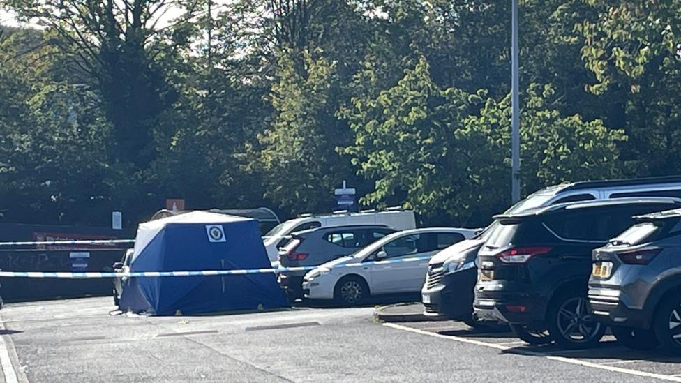 A blue police tent and cordon next to a row of cars