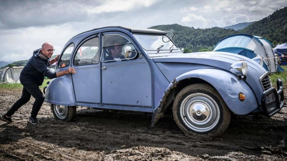 A man pushes a car out of the mud during the 24th World meeting of Citroen 2CV friends near Delemont, northern Switzerland on July 26, 2023.