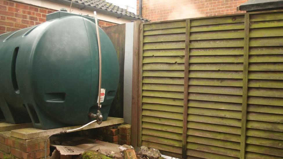 A large green plastic tank with a tap, housed in a garden.
