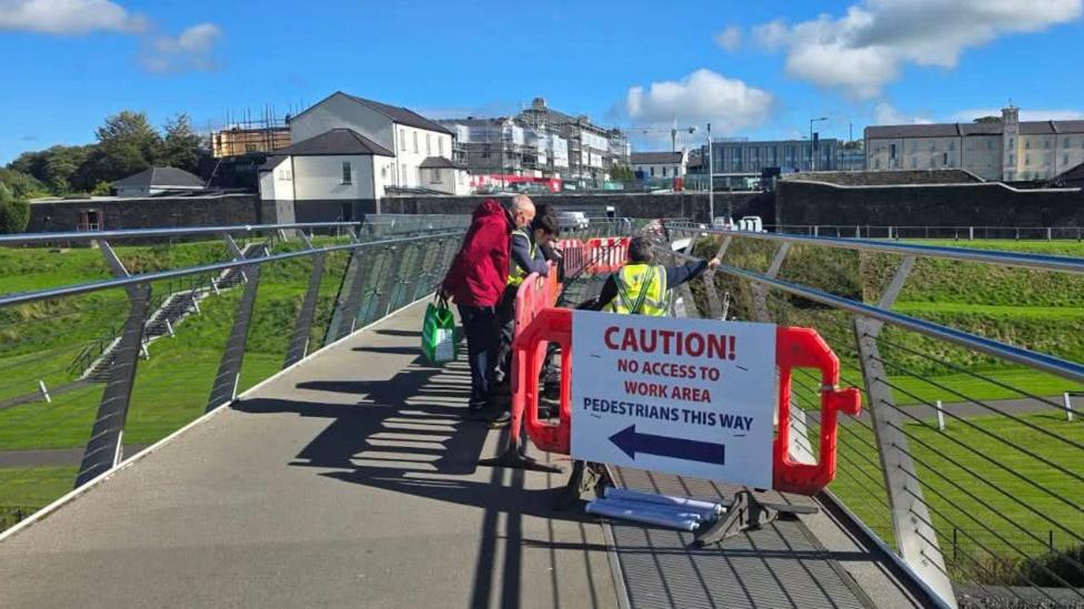 A diversion sign advising pedestrians that no access is aviable sits on Derry's peace bridge. A member of the public is talking to a workman