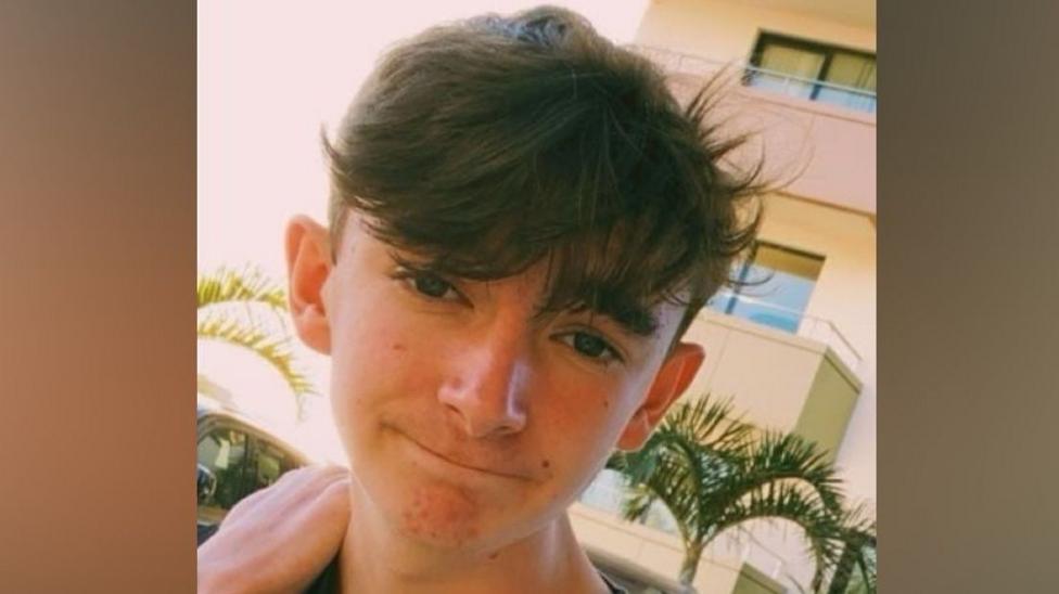 Jamie Collins smiling at the camera on holiday, with an apartment block in the background.