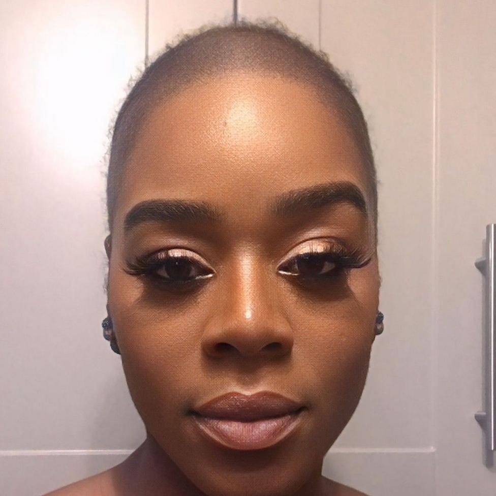 A selfie of Antonia. She is looking straight into the camera and her head is bald. She is wearing light eye shadow, lashes, and a neutral lipstick.