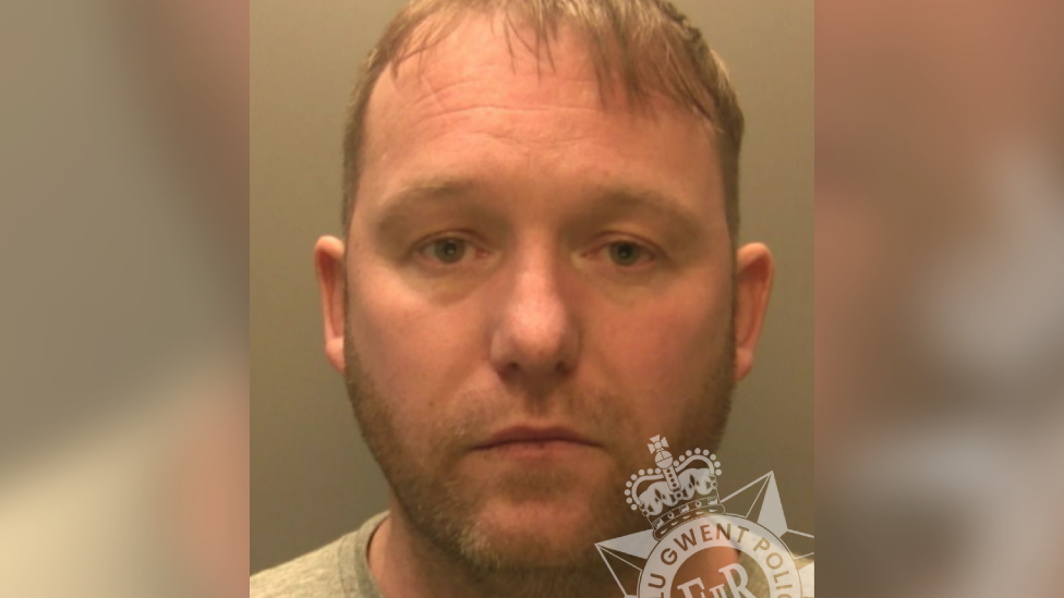 Custody shot of Martin Newman. He has short blond hair and short stubble. He wears a grey t-shirt.