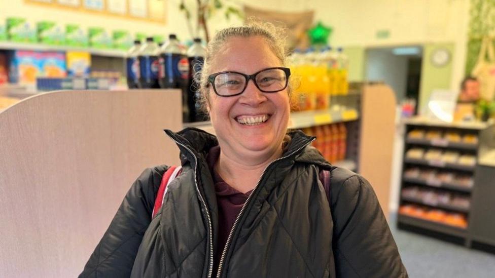 A women in a black jacket with a smile. She is stood in the store.