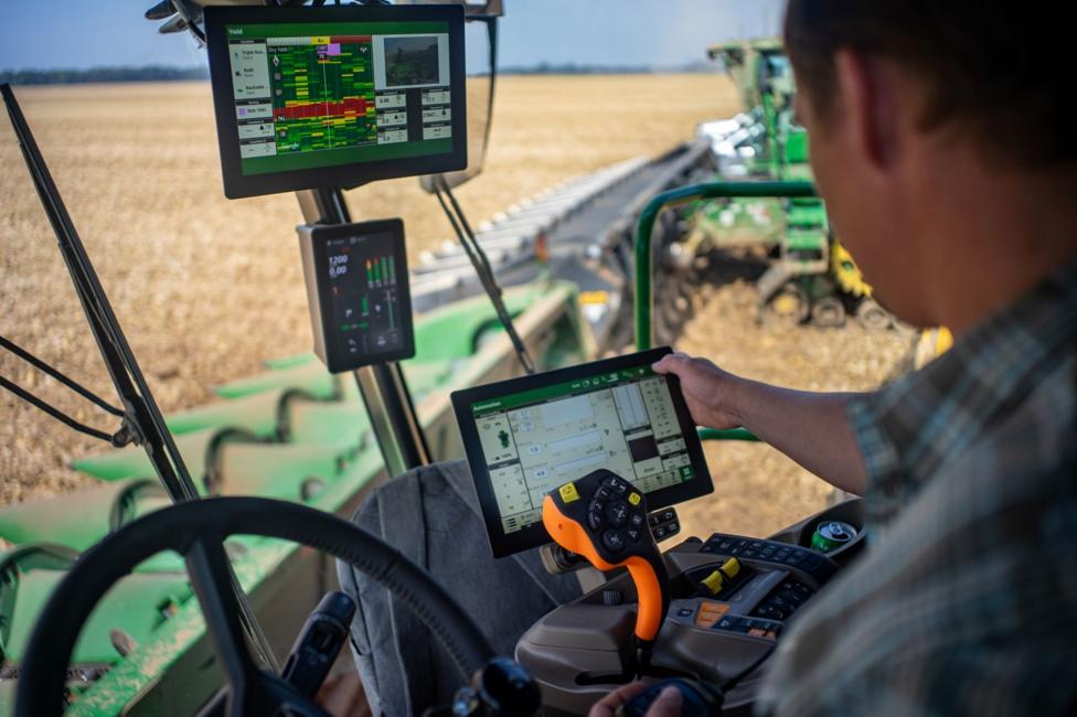 A farmer programmes a computer inside the cab of a combine harvester. It is working a wheat field.