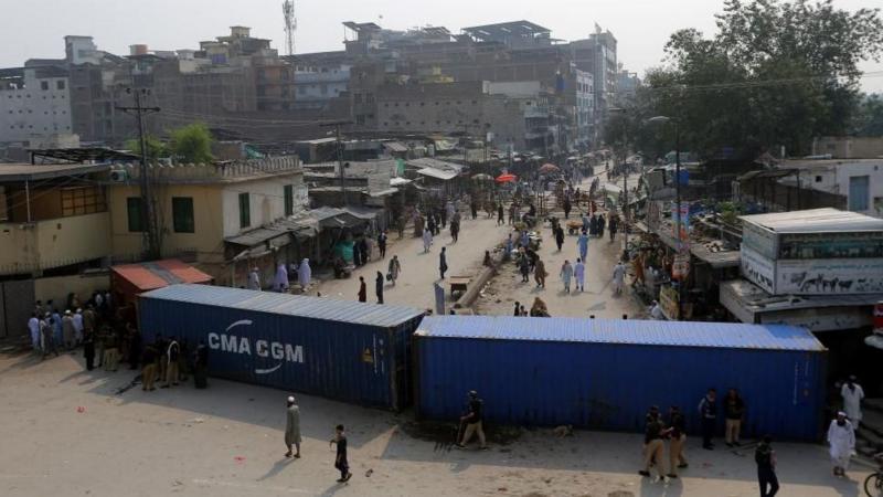 Two large blue shipping containers block a busy wide street