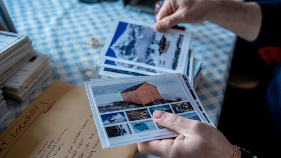 A person's hand holds a selection of postcards showing images of the Antarctic base.