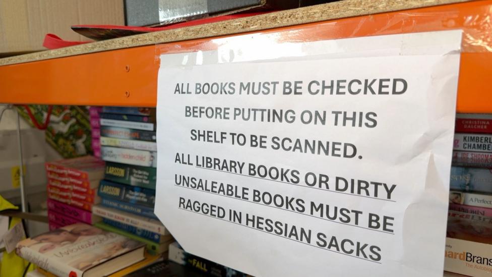 A paper notice reads: All books must be checked before putting on this shelt to be scanned. All library books or dirty unsaleable books but be ragged in hessian sacks. 
