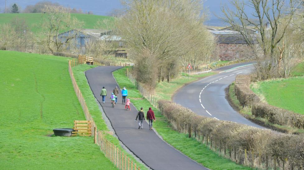 An aerial view of a cycle path running next to a road through the rural countryside of southern Scotland