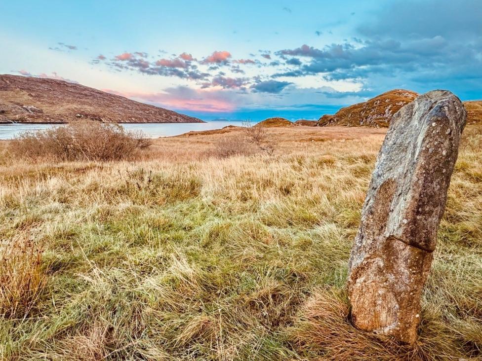 A standing stone with a loch and hills in the background
