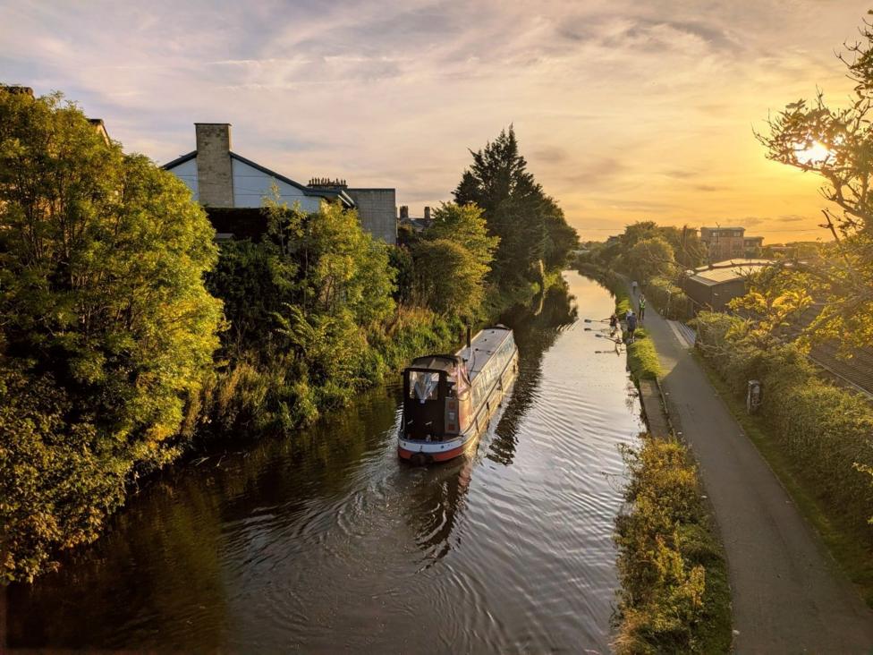 A narrow boat sails down a canal with trees on either side