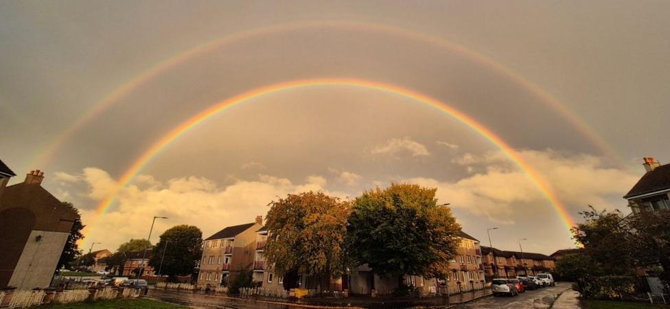 A wide photo of a double rainbow over a residential street