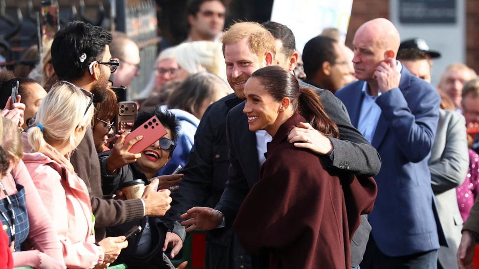 Prince Harry puts his arm round Meghan's shoulder as they talk to fans.