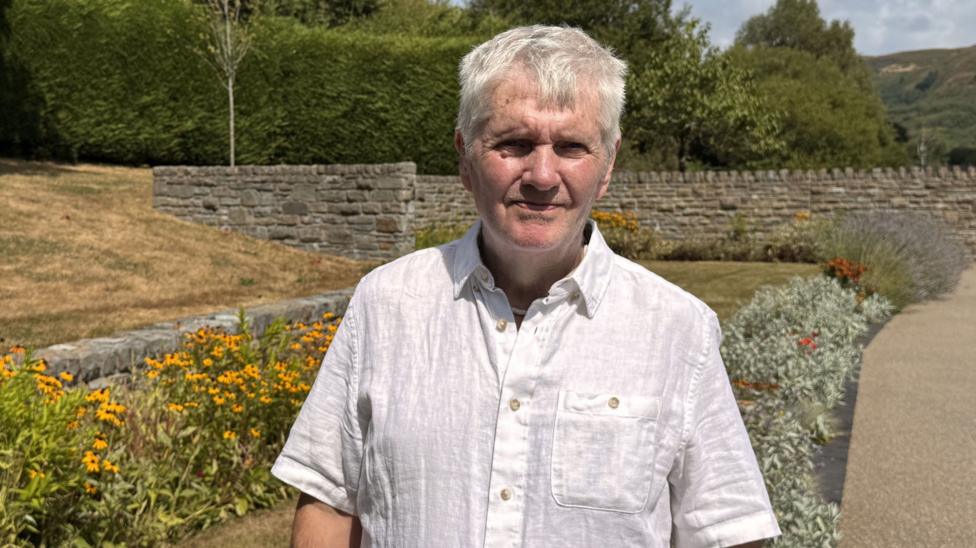 A man in a white shirt next to a field of flowers