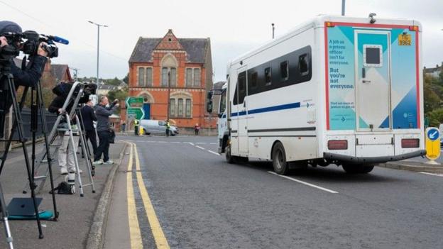 Donaldson leaving Newry court in a prison van after being sentenced on Thursday. To the left of the van are media. To the front of the picture is a red building. And on the back of the van is an advertisement for prison staff.