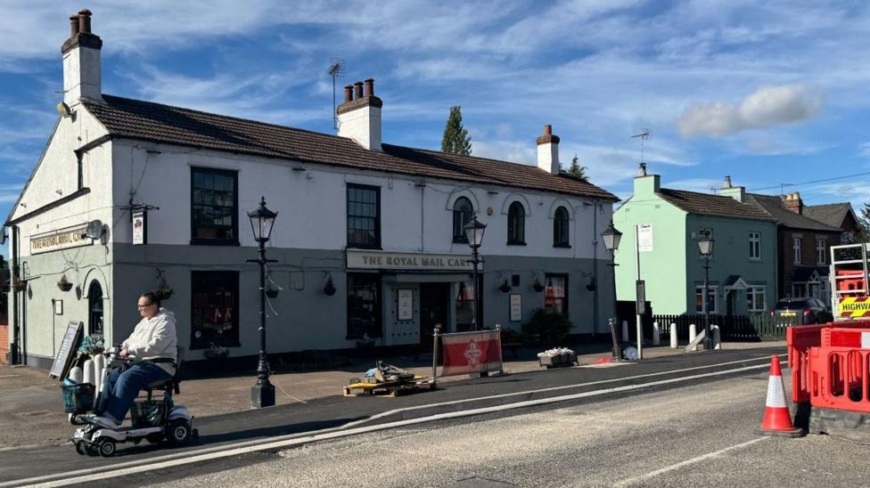 A photograph of The Royal Mail Cart pub from the outside. It is a green and white building with a road directly outside.