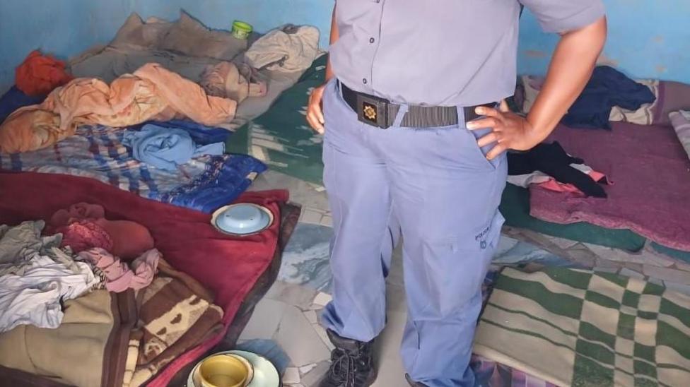 A police officer stands in a room where multitudes were found at an illegal rehab centre in South Africa